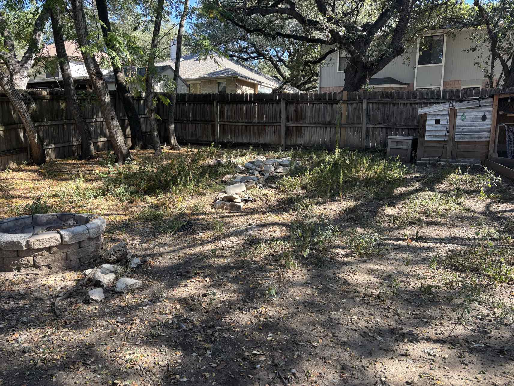 Overgrown backyard with weeds rocks and fire pit before yard cleanup by Urban Landscaping San Antonio