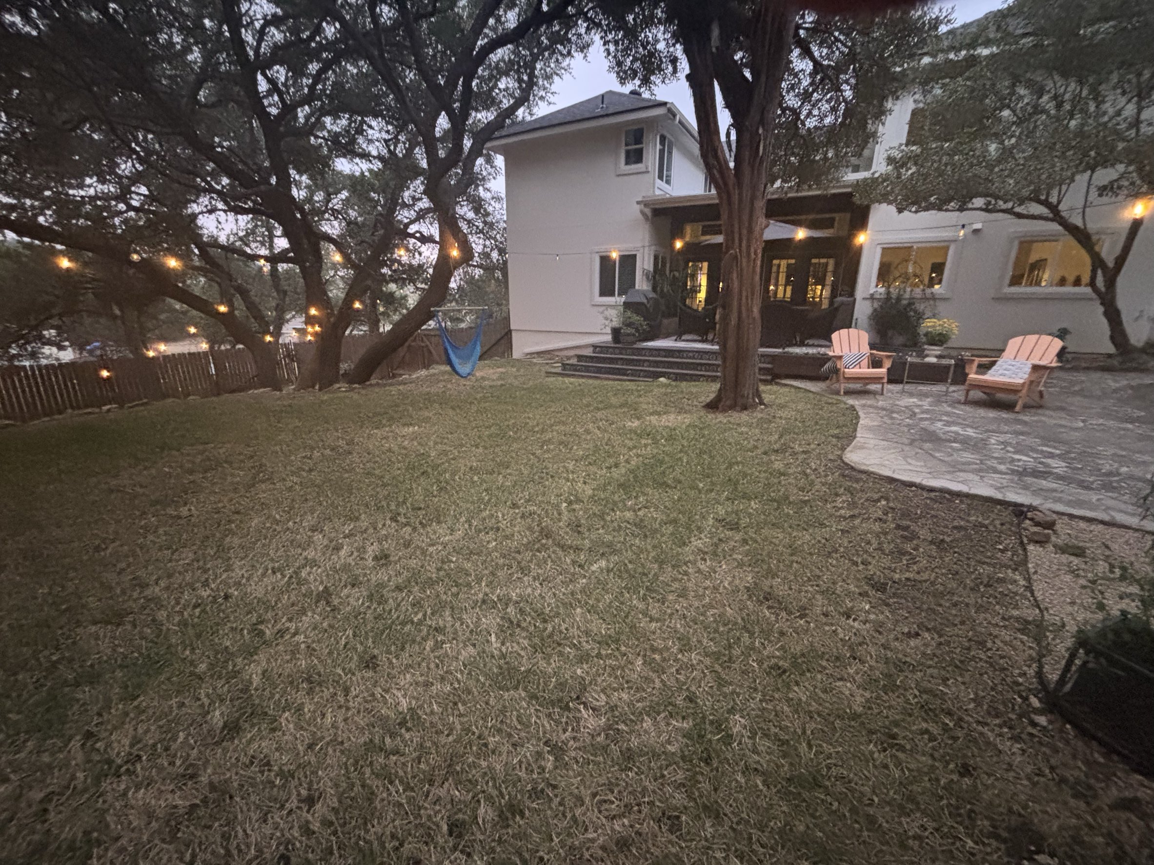 Maintained backyard with mowed lawn under mature oak trees and patio area by Urban Landscaping San Antonio