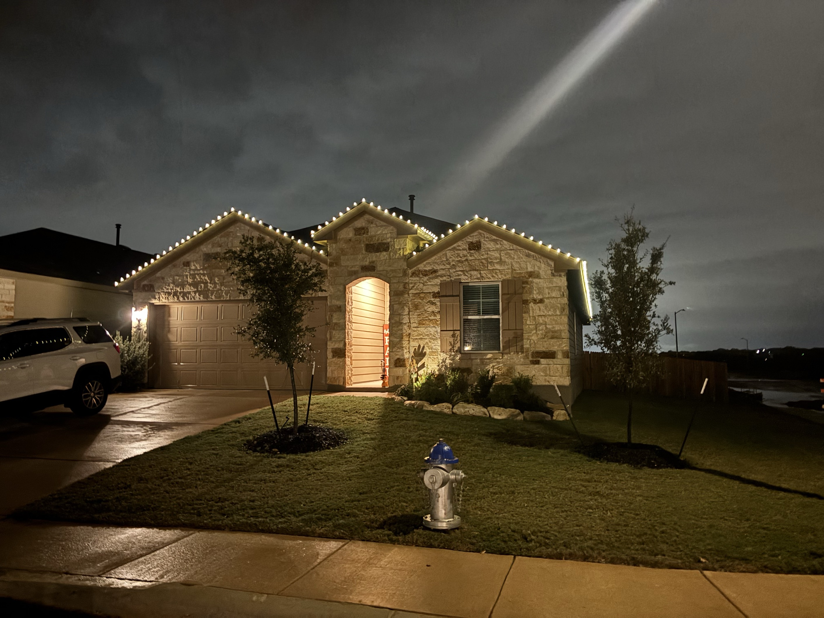 Same single story stone home with warm white Christmas lights installed along roofline at night by Urban Landscaping San Antonio