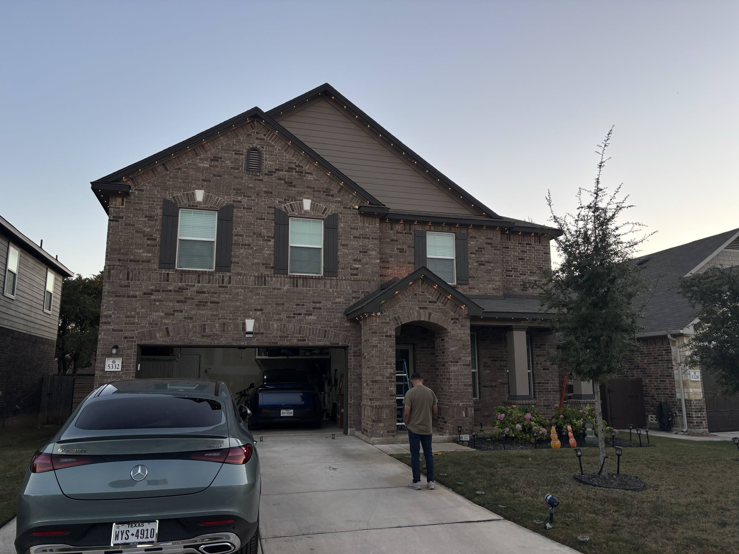 Two story brick home at dusk during holiday light installation by Urban Landscaping San Antonio