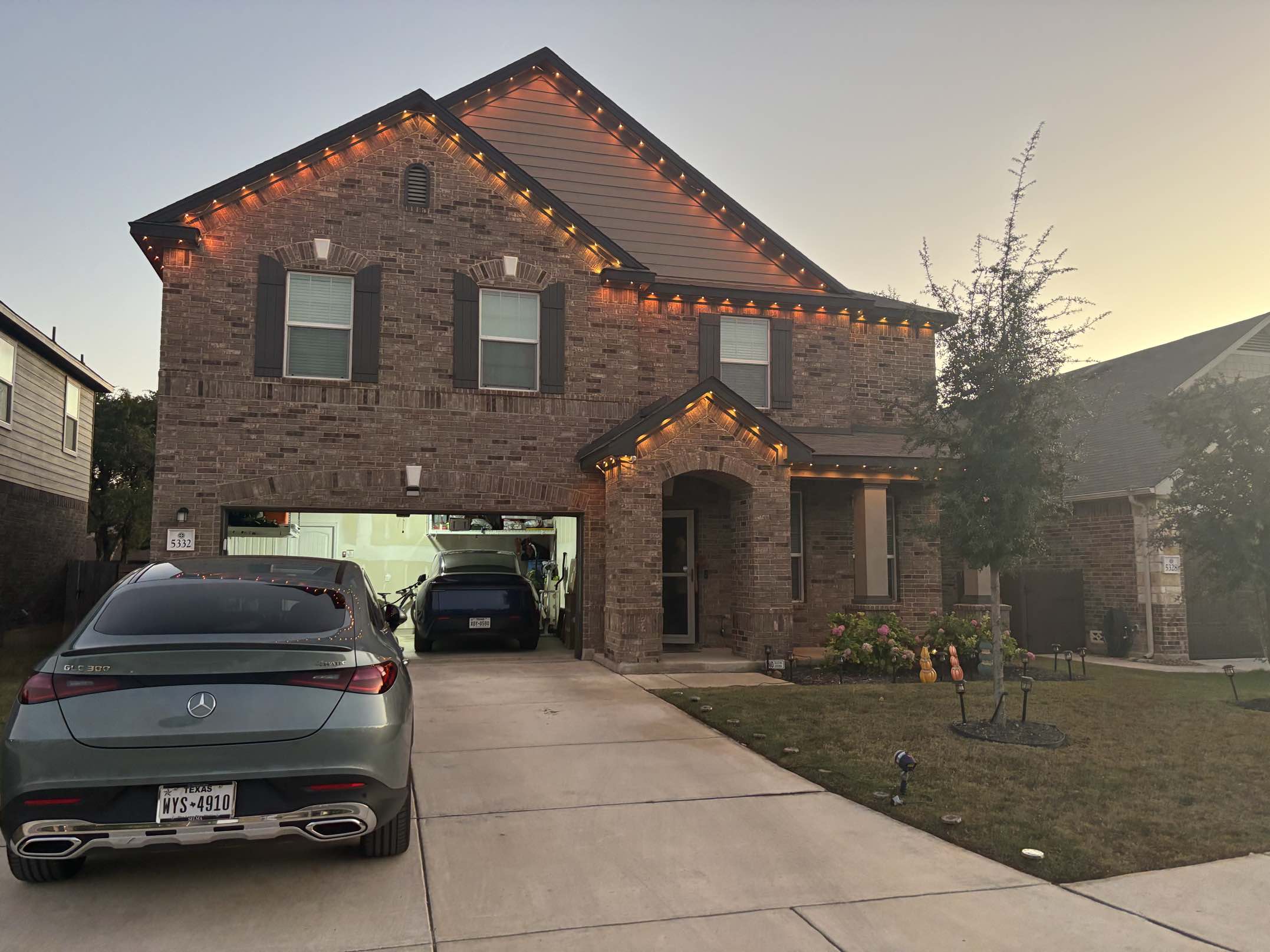 Same two story brick home with warm glowing holiday lights fully installed at twilight by Urban Landscaping San Antonio